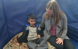 Upset child sitting on cushion next to therapist