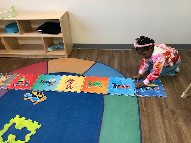 Child sitting on a colorful rug putting together a Pete the Cat puzzle.