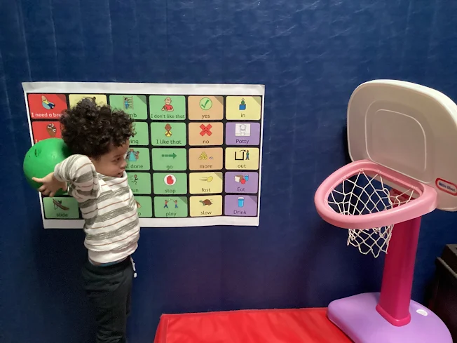 Child throwing a ball into a basketball hoop in Blue Bird Day's sensorimotor gym