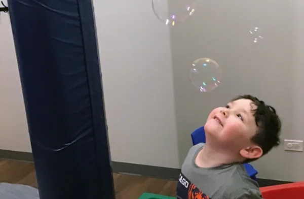 Boy in Blue Bird Day classroom blowing bubbles for calming sensory input